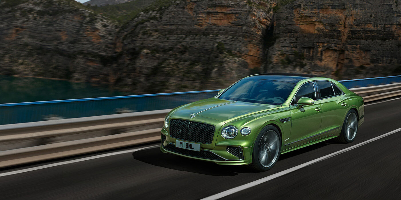 Bentley Beirut Bentley New Flying Spur Speed v8 hybrid sedan driving dynamically on a mountain road in Tourmaline Green paint