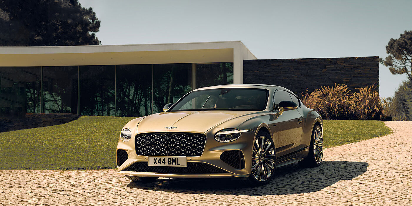 Bentley Beirut Bentley Continental GT Mulliner coupe front three quarters in Patina paint parked outside a glass fronted building with a grass lawn behind it