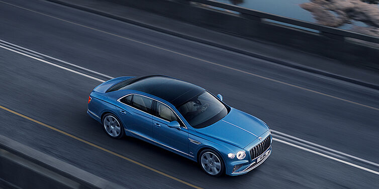 Bentley Beirut New Bentley Flying Spur Azure sedan in Light windsor blue paint by Mulliner, with 22 inch Azure wheels seen from overhead driving dynamically on a country road