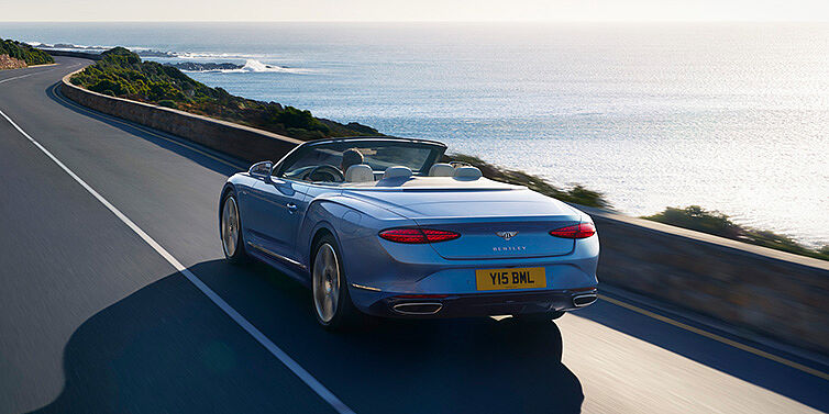 Bentley Beirut New Bentley Continental GTC Azure convertible rear view in Light Windsor blue paint with 22 inch ten spoke wheels driving dynamically on an ocean road in the sunshine