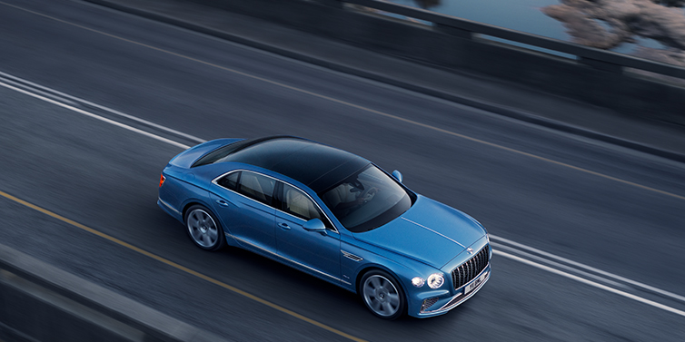 Bentley Beirut New Bentley Flying Spur Azure sedan in Light windsor blue paint by Mulliner, with 22 inch Azure wheels seen from overhead driving dynamically on a country road