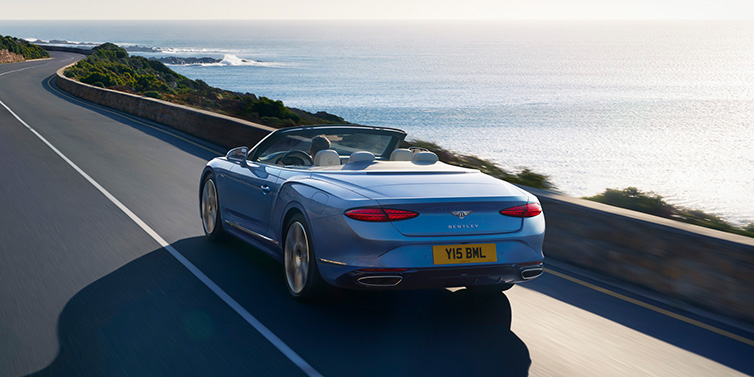 Bentley Beirut New Bentley Continental GTC Azure convertible rear view in Light Windsor blue paint with 22 inch ten spoke wheels driving dynamically on an ocean road in the sunshine