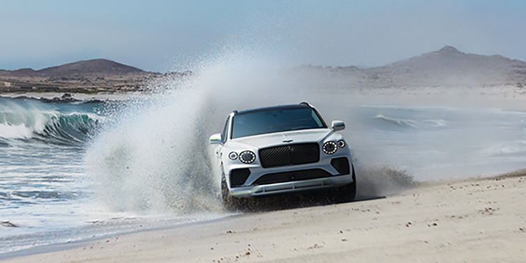 Bentley Beirut Bentley Bentayga Speed SUV facing front in Snow Quarts Pearlescent white paint driving dynamically on beach