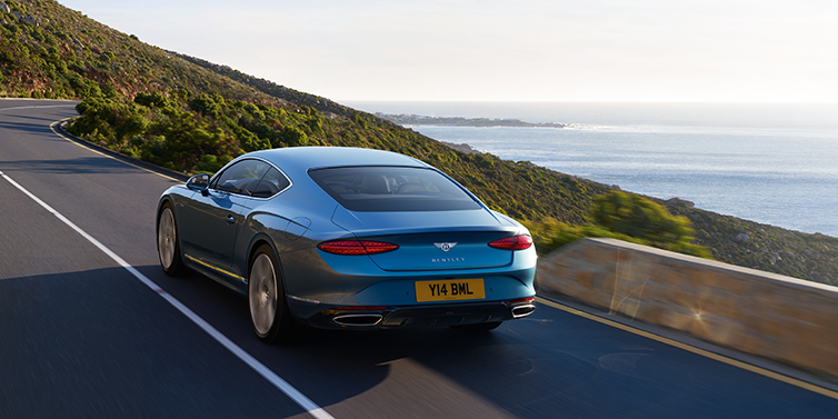 Bentley Beirut New Bentley Continental GT Azure coupe in Light Windsor blue paint seen from the rear driving dynamically on a seaside road